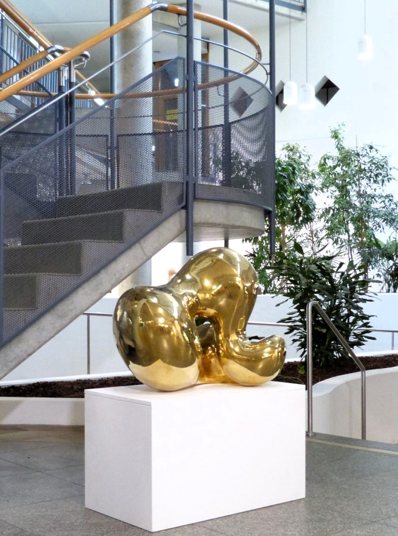 Abstract polished brass sculpture with round, organic forms, placed in a lage open foyer.