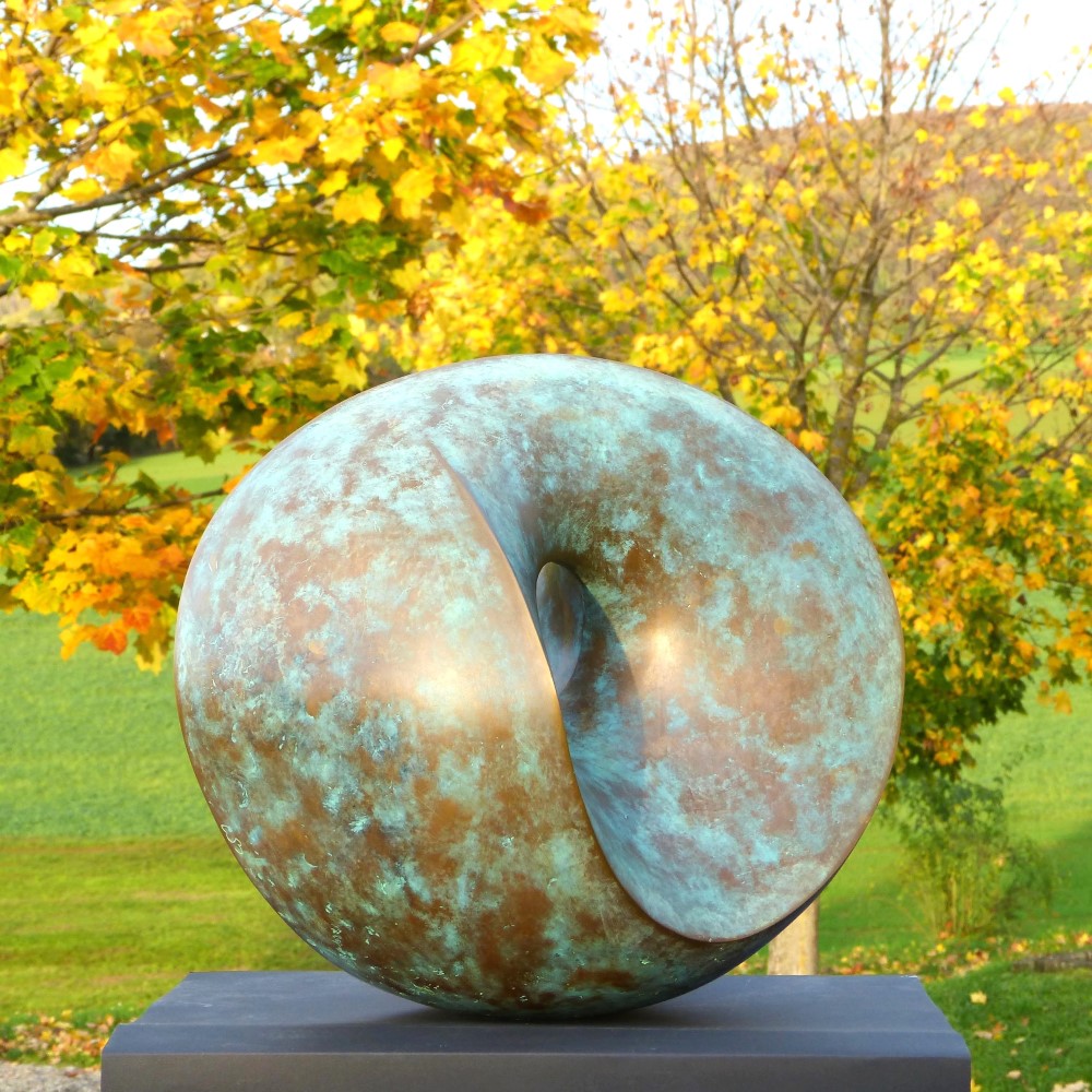 Abstrakte, runde Skulptur aus matt geschliffener, goldleuchtender Siliziumbronze.